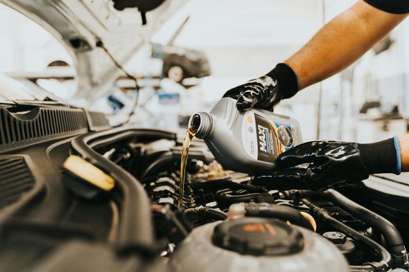Mechanic pouring motor oil into a car engine, wearing black gloves, in a garage.