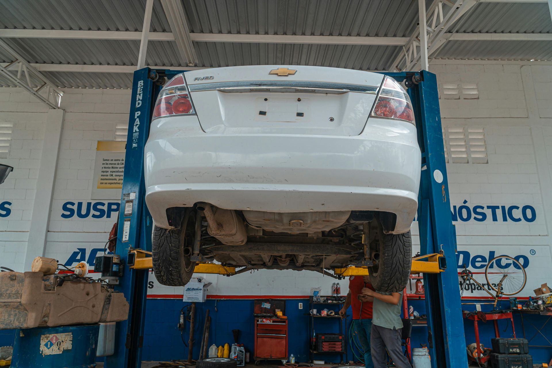 White car raised on a lift in a garage. Mechanic is working underneath the car.