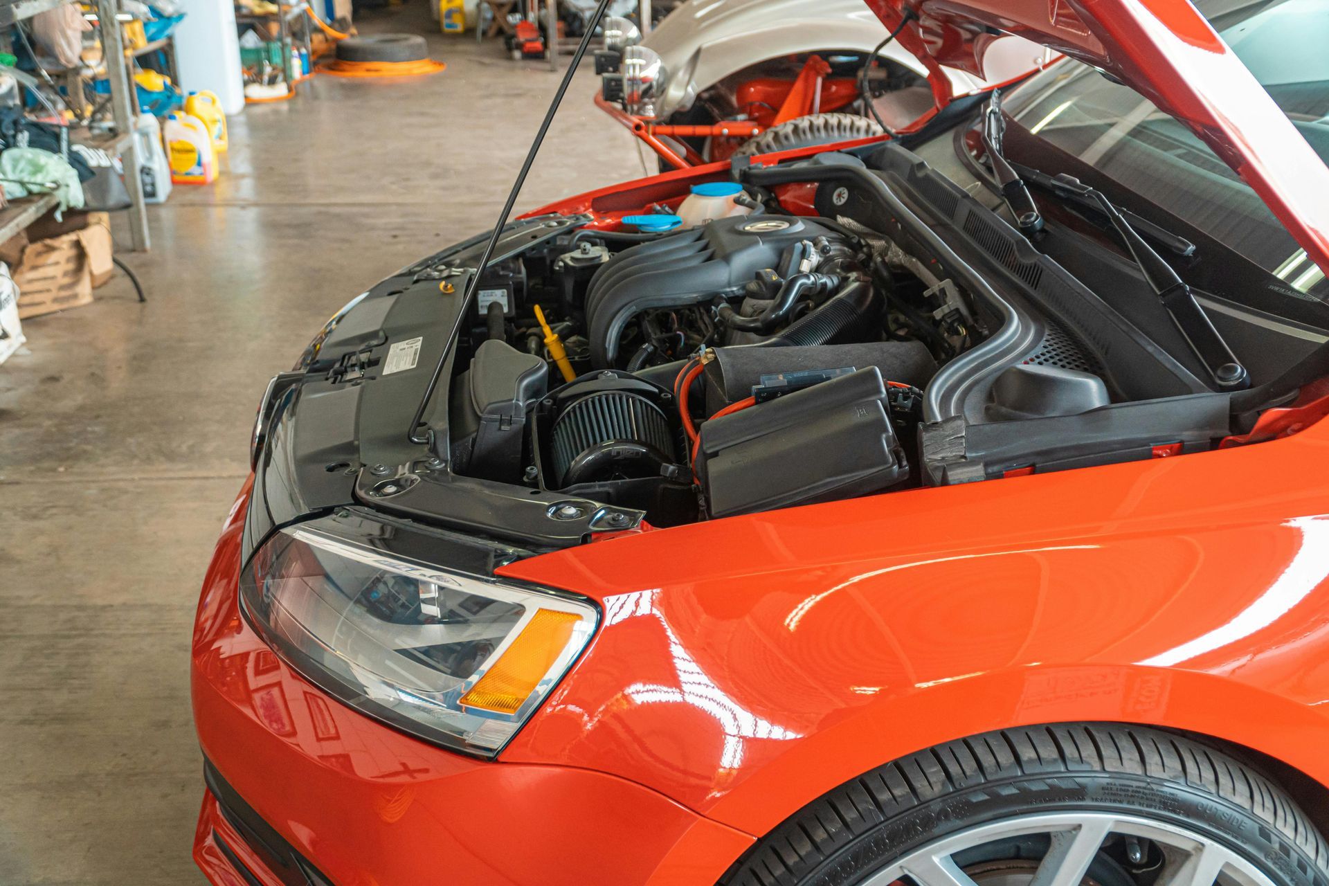 Red car with the hood open, engine visible in a garage setting.