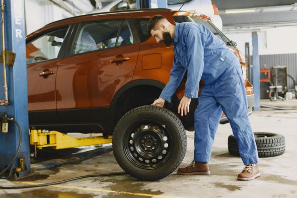 Mechanic in blue jumpsuit, holding a tire, working on a red car in a garage.