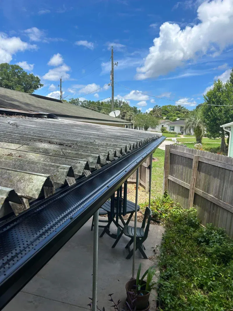 A patio with a table and chairs under a roof with a black gutter.