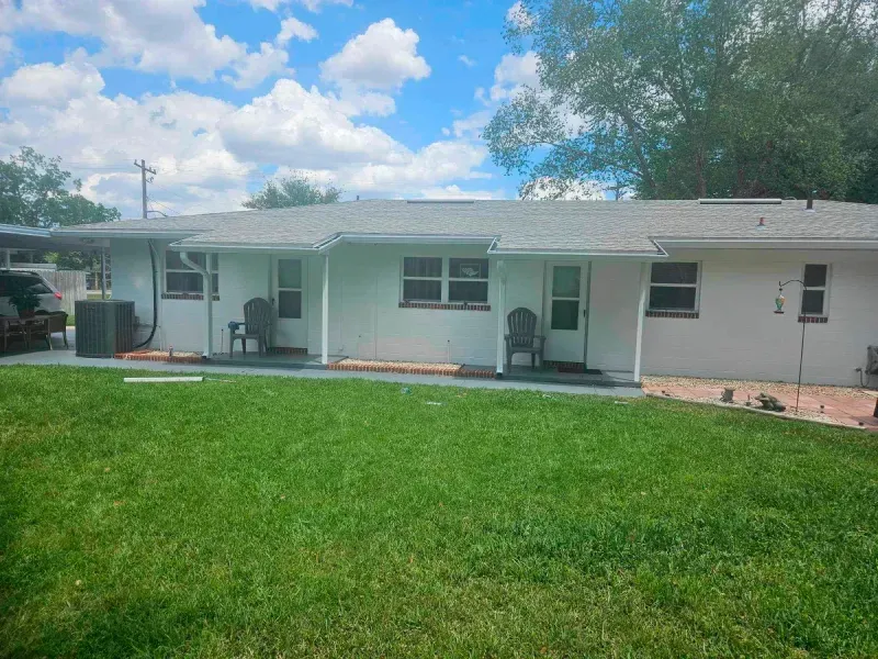 A white house with a gray roof and a large lawn in front of it.