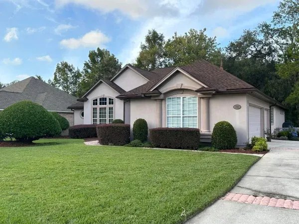A white house with a brown roof and a lush green lawn