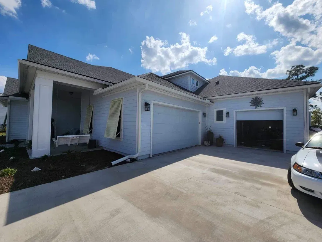 A white car is parked in front of a white house.