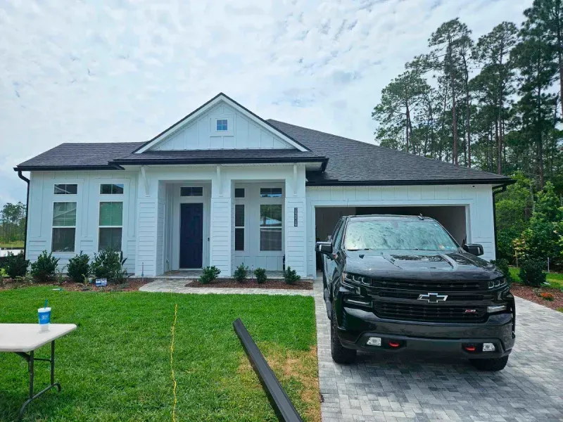 A black truck is parked in front of a white house.