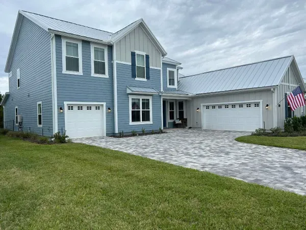 A large blue and white house with two garages and an american flag in front of it.