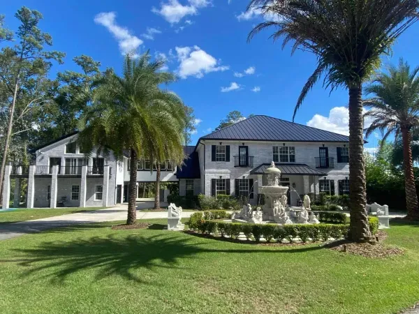 A large white house with a fountain in front of it surrounded by palm trees.