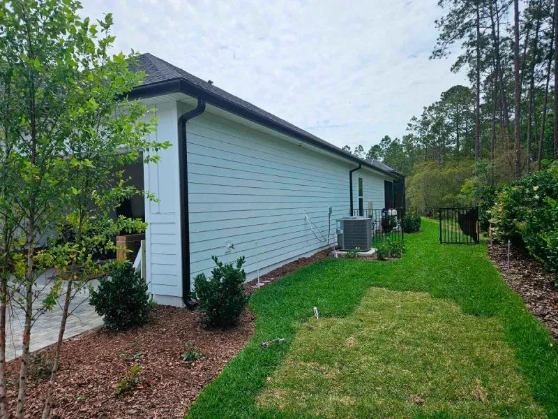 The backyard of a house with a lush green lawn and trees.