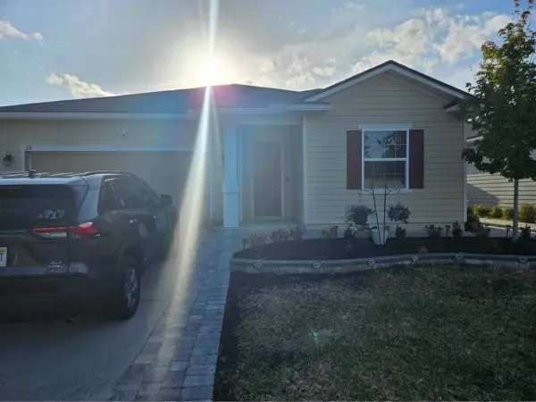 A car is parked in front of a house with the sun shining through the windows.