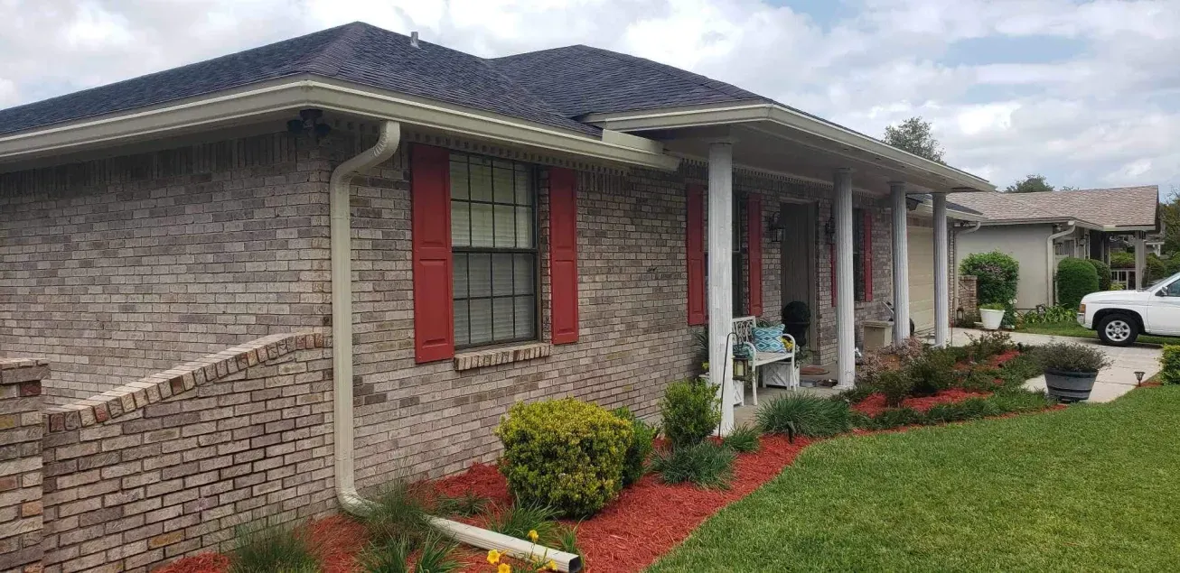 A brick house with red shutters and a car parked in front of it.