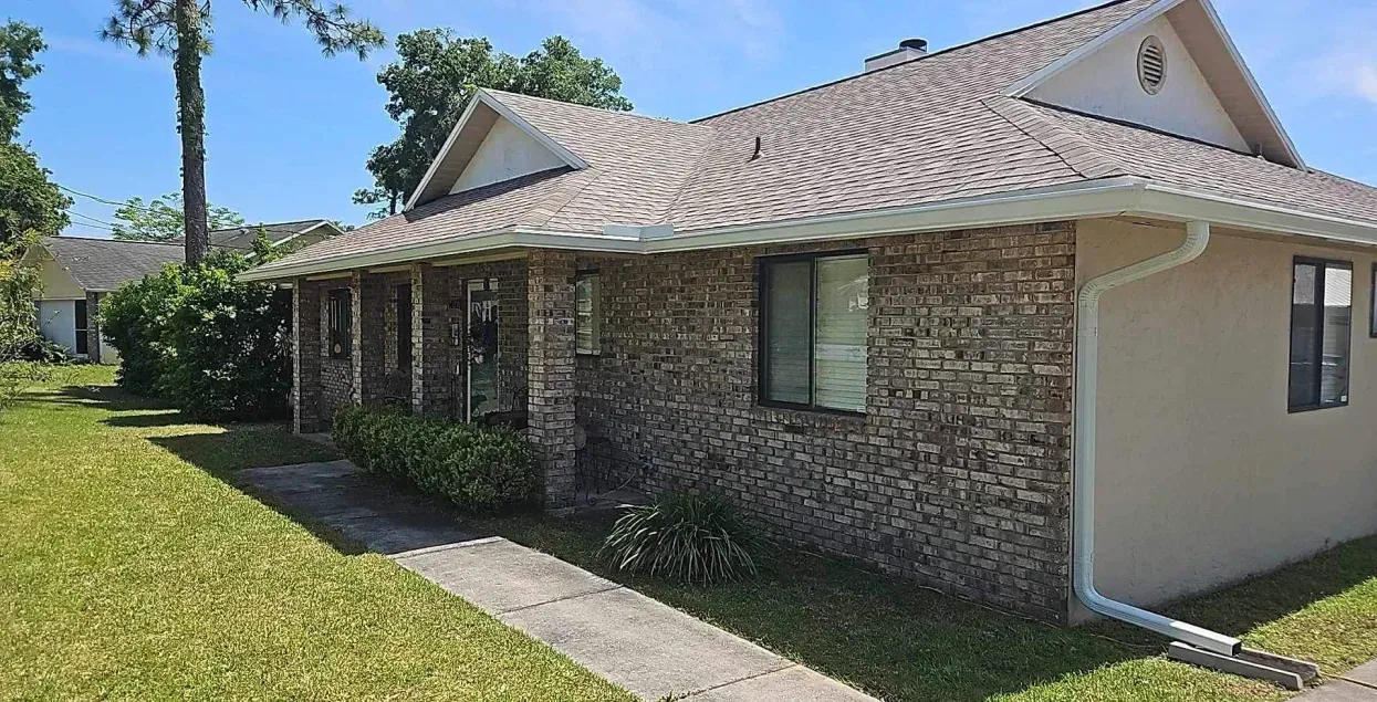 A small brick house with a roof and a walkway leading to it.