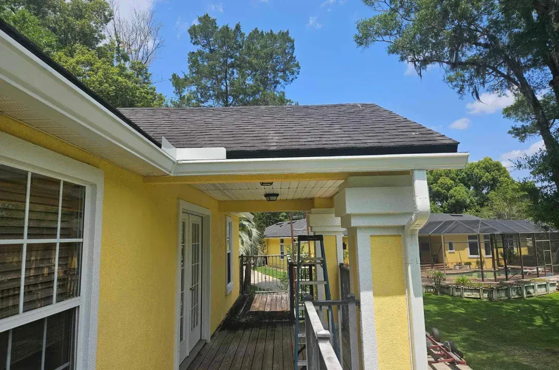 A yellow house with a porch and trees in the background.