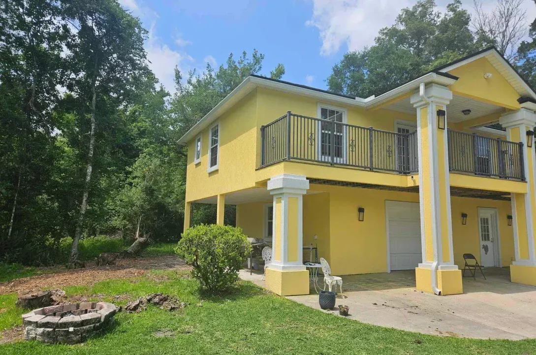 A large yellow house with a balcony and a fire pit in front of it.