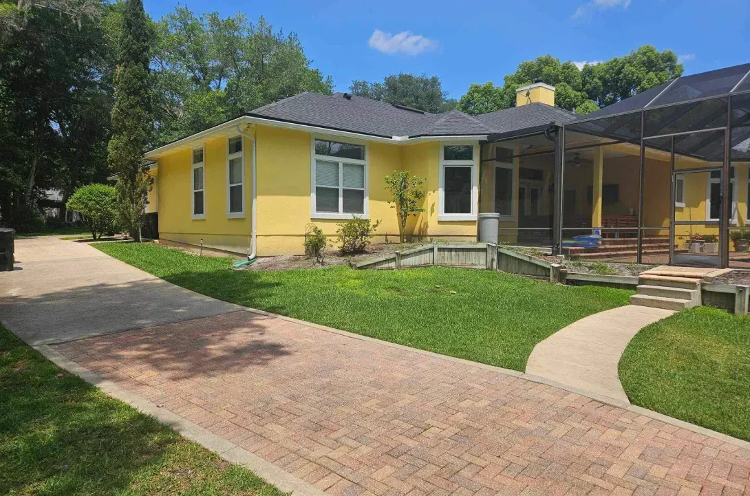 A yellow house with a brick walkway leading to it.