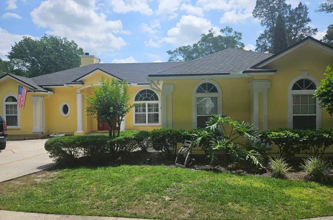 A yellow house with a black roof and a car parked in front of it.