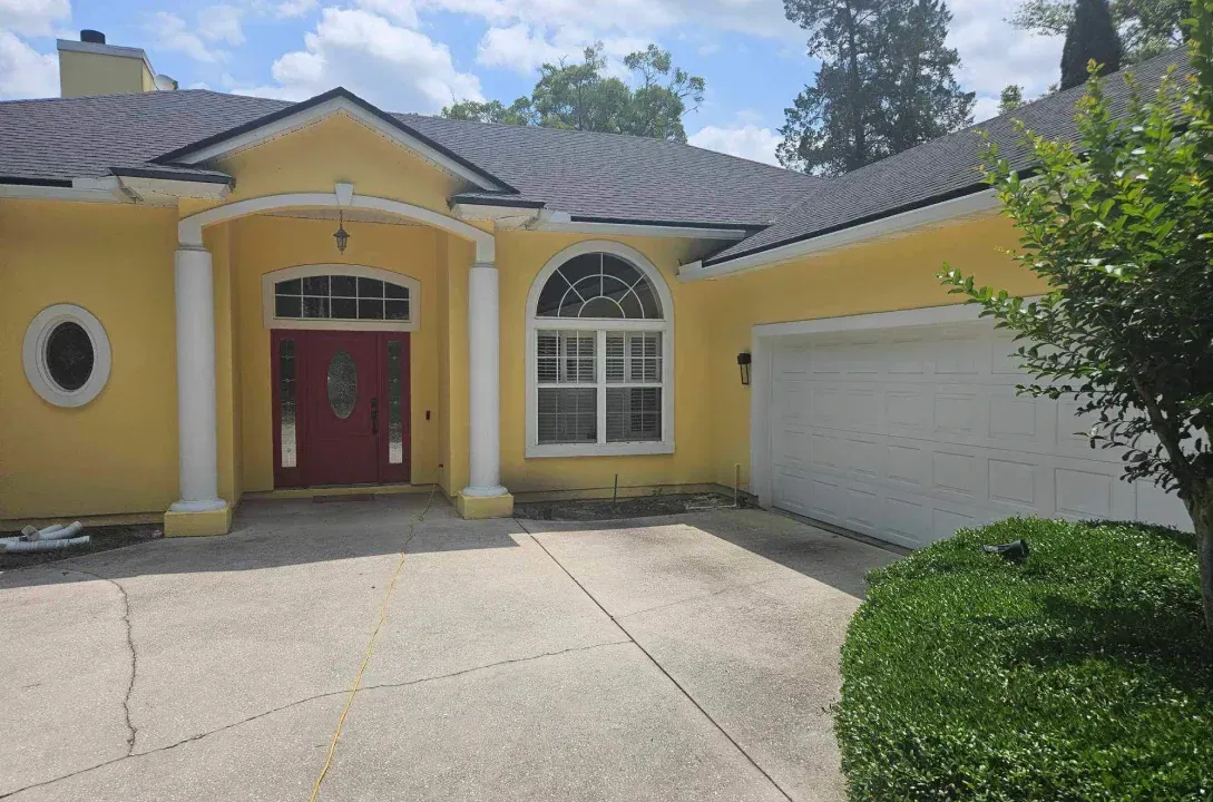 A yellow house with a red door and a white garage door.
