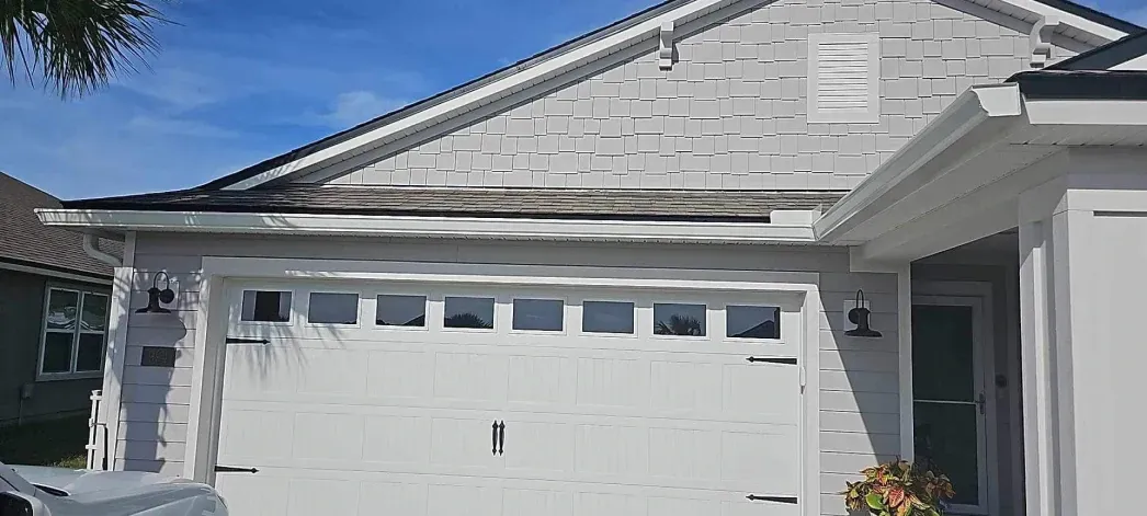 A white house with a white garage door and a blue sky in the background.