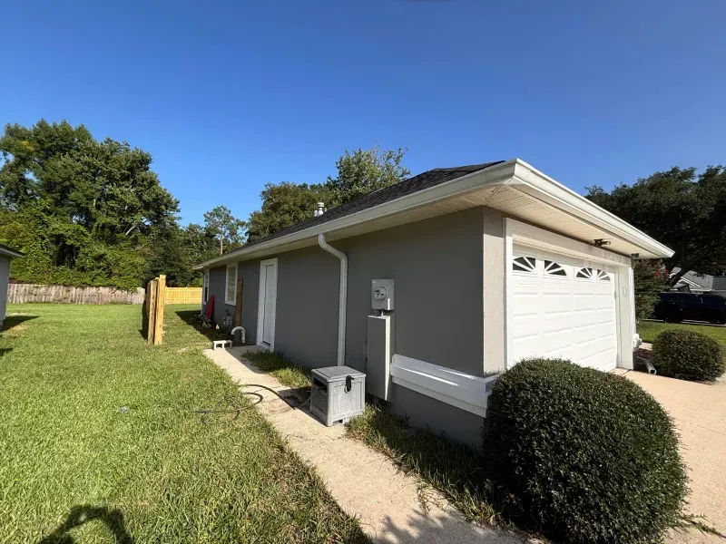 A small house with a garage and a sidewalk in front of it.