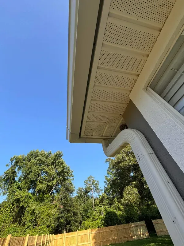 A gutter on the side of a house with a fence in the background.