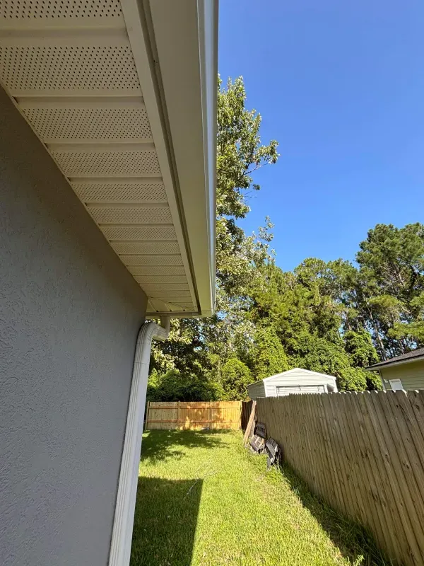 A house with a gutter on the side of it and a fence in the backyard.