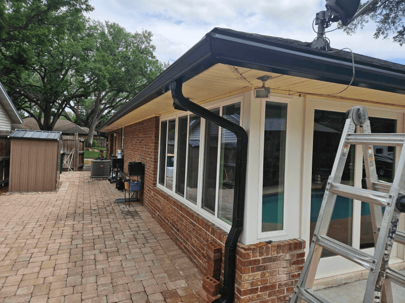 A house with a black gutter and a ladder in front of it.