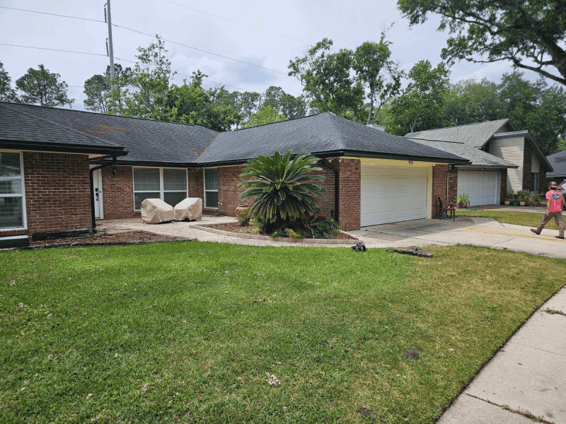 A man is standing in front of a brick house with a black roof.