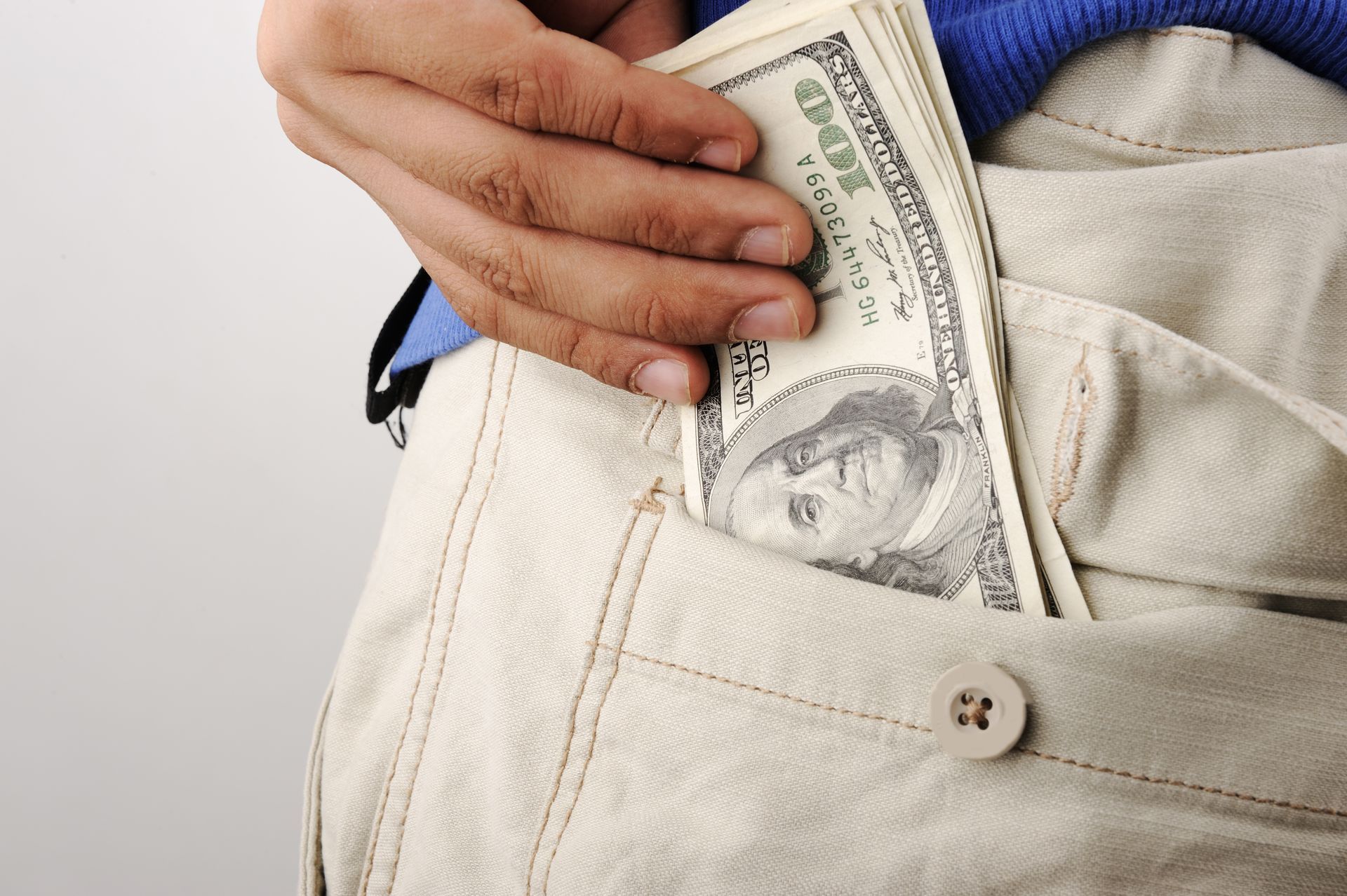 Hand pulling a stack of $100 bills from a tan pants pocket.