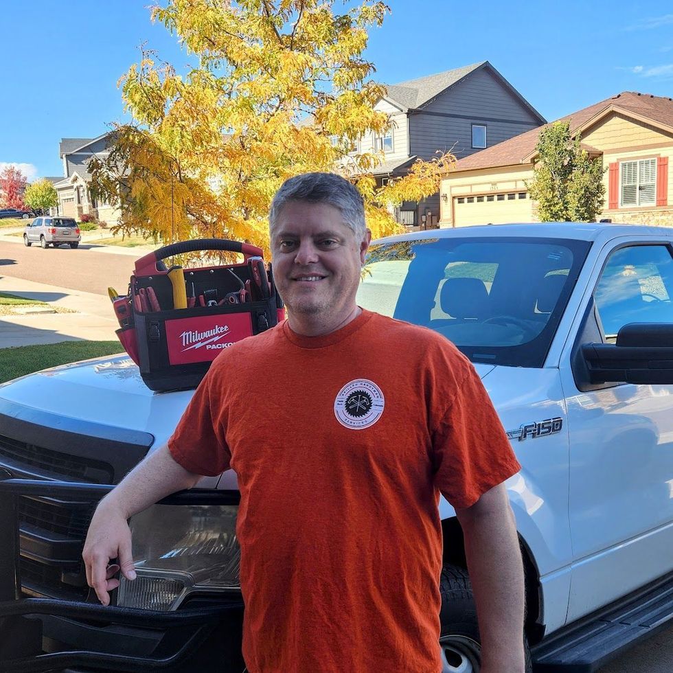 A man in an orange shirt is standing next to a white truck.