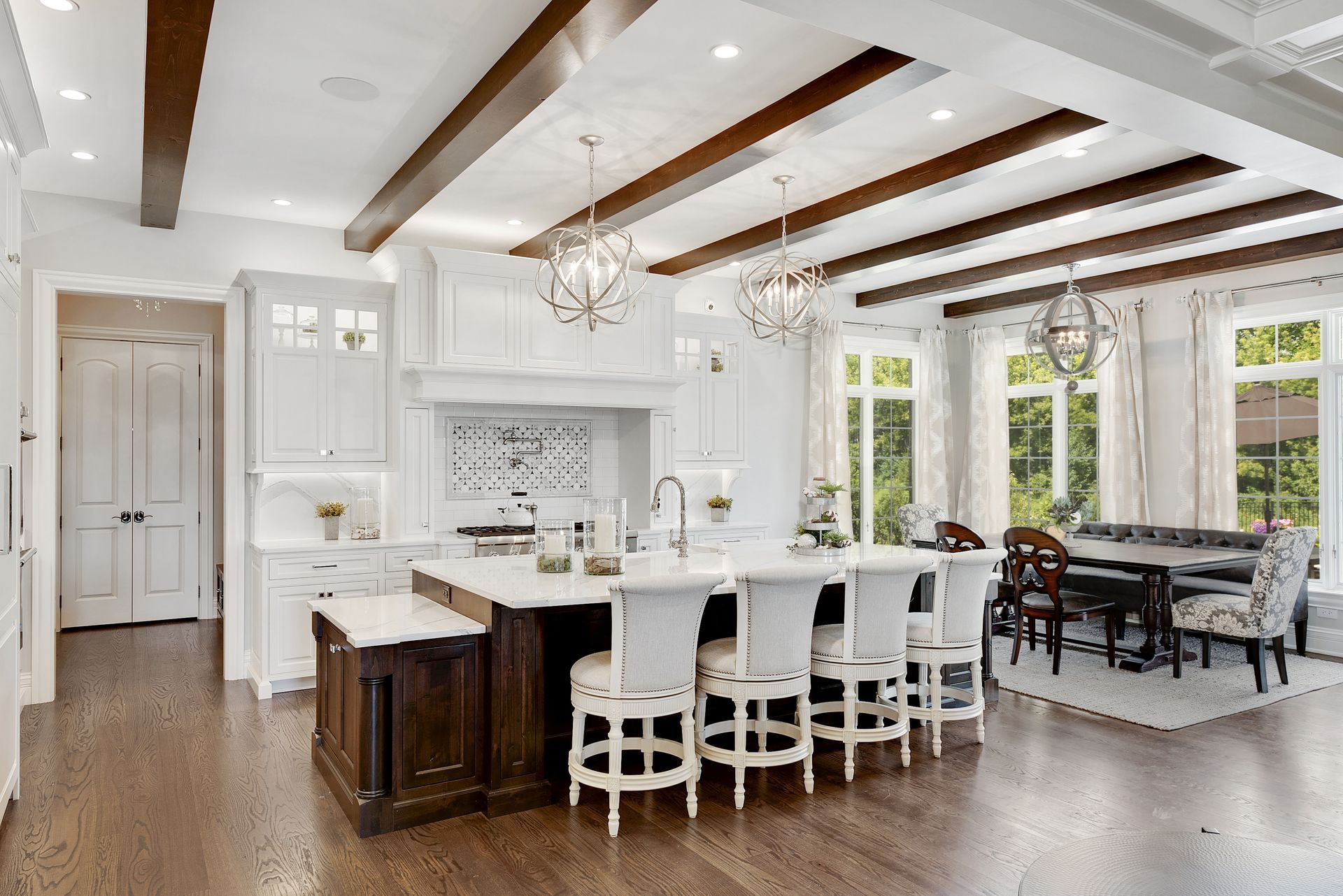 Elegant white kitchen with dark island and wooden beams, breakfast bar, dining area.