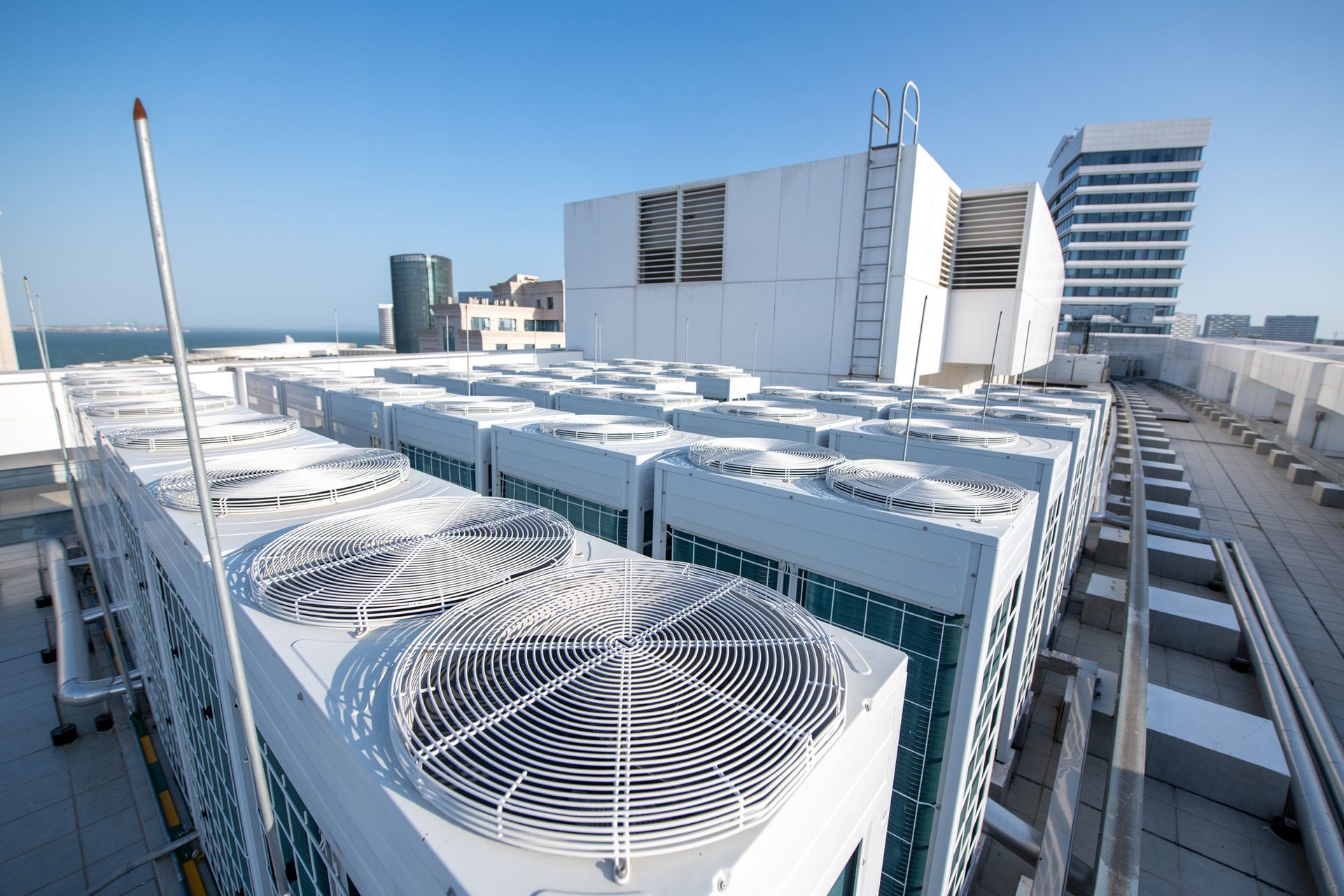 Rooftop view of air conditioning units on a building, with city skyline in the background under a blue sky.
