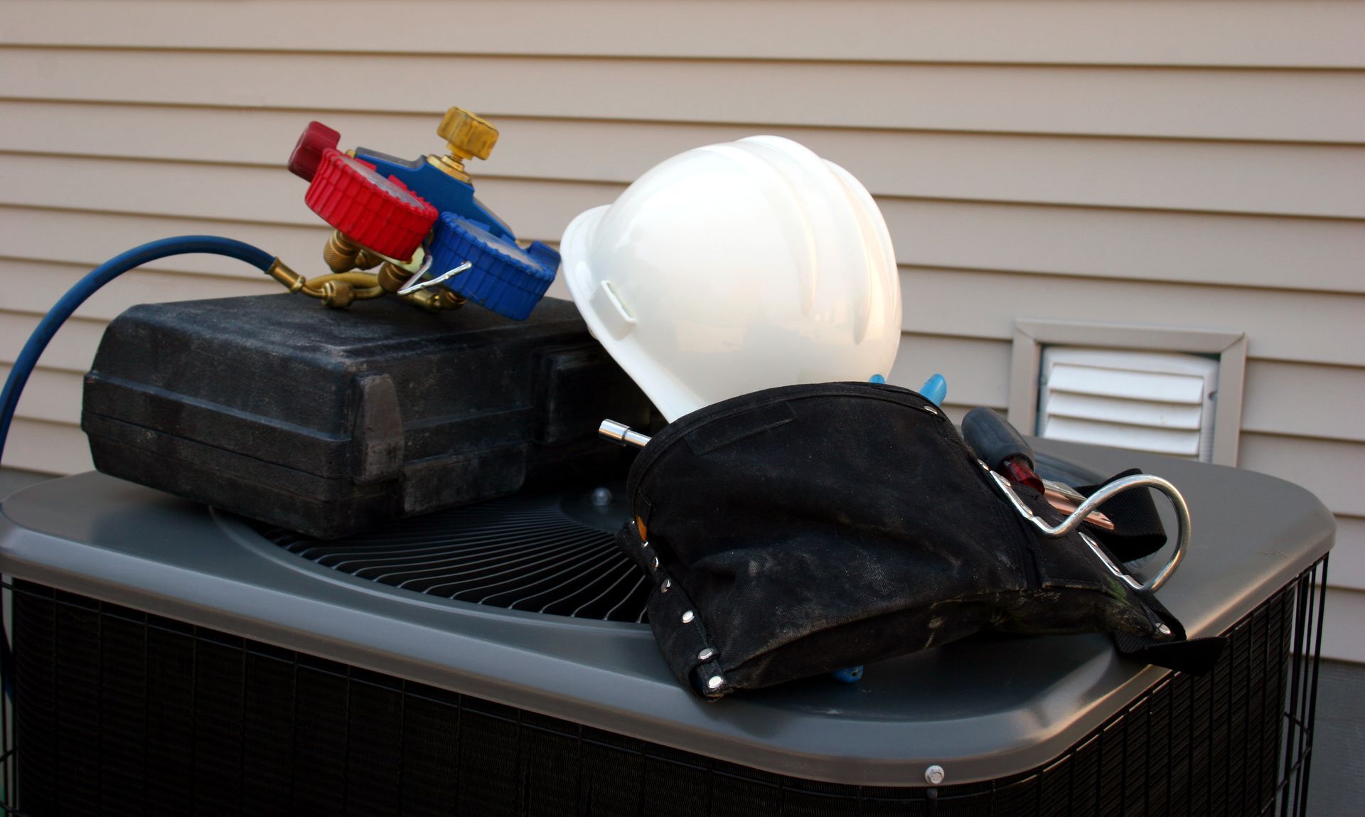 HVAC tools and white hard hat on top of an air conditioning unit outside a building.