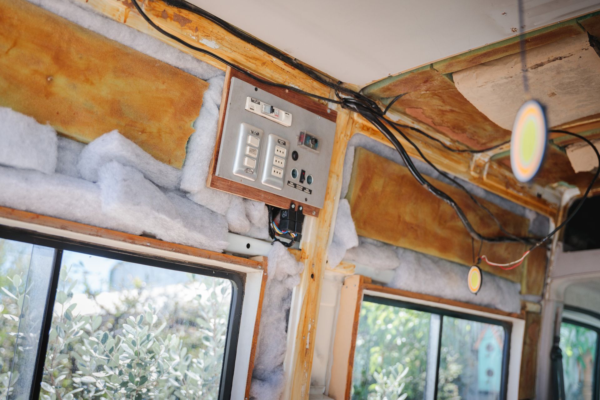 Interior of a vehicle with exposed framing, insulation, and control panel. Windows and wires visible.