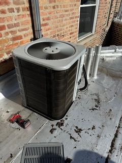 Air conditioning unit on a rooftop next to a brick building. A power tool sits nearby.