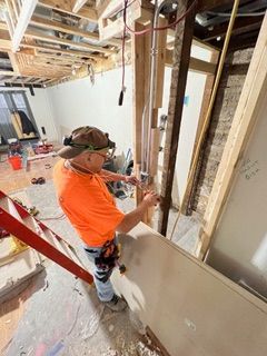 Plumber in gray overalls using a wrench to connect a hose to a water heater.