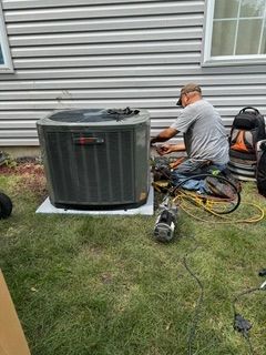 HVAC technician in orange jumpsuit repairs AC unit outside, using gauges.