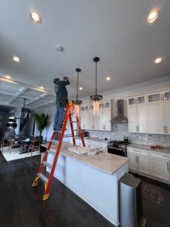 Electrician cutting wires, wearing hard hat, safety glasses, gloves, and plaid shirt.