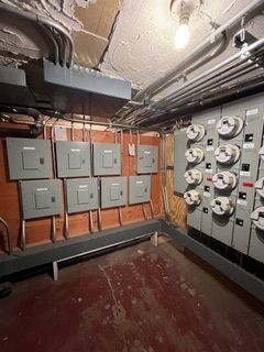 Electrical panels and meters in a utility room. Gray boxes on wood paneling and red floor.