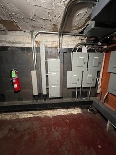 Electrical panels and conduit mounted on a dark wall in a room with a red floor; fire extinguisher on the wall.