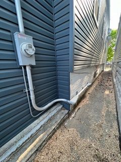 Electrical meter on blue siding of a building, next to a narrow concrete path with a gravel ground.