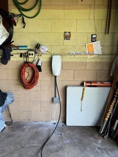 Garage interior with an electric vehicle charger, orange extension cord, and white folding table.