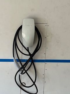 White Tesla charger mounted on a wall with a coiled black charging cable.