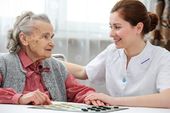 Elderly woman playing a board game with her carer