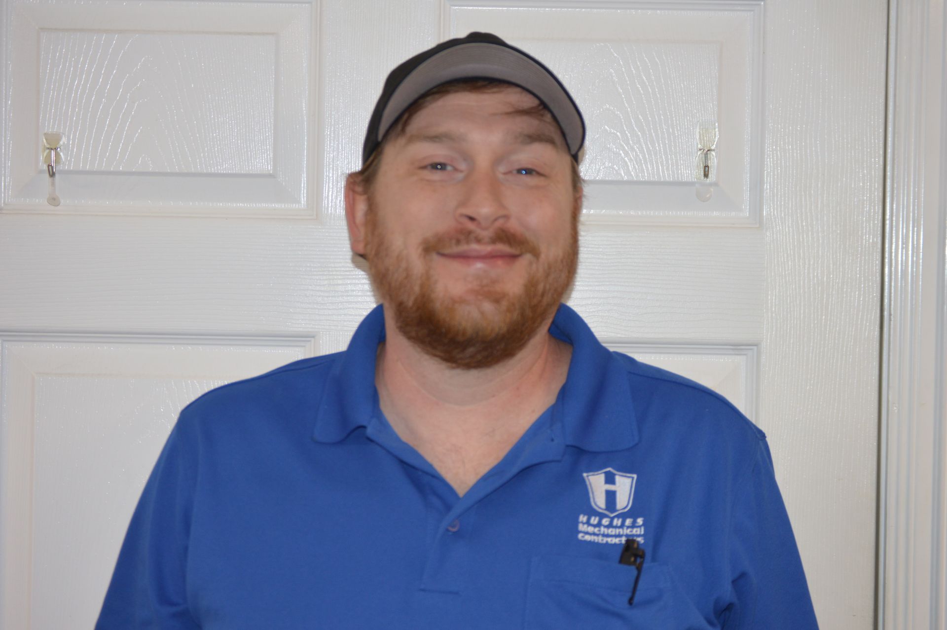 Man in a blue polo and cap smiles in front of a white door.