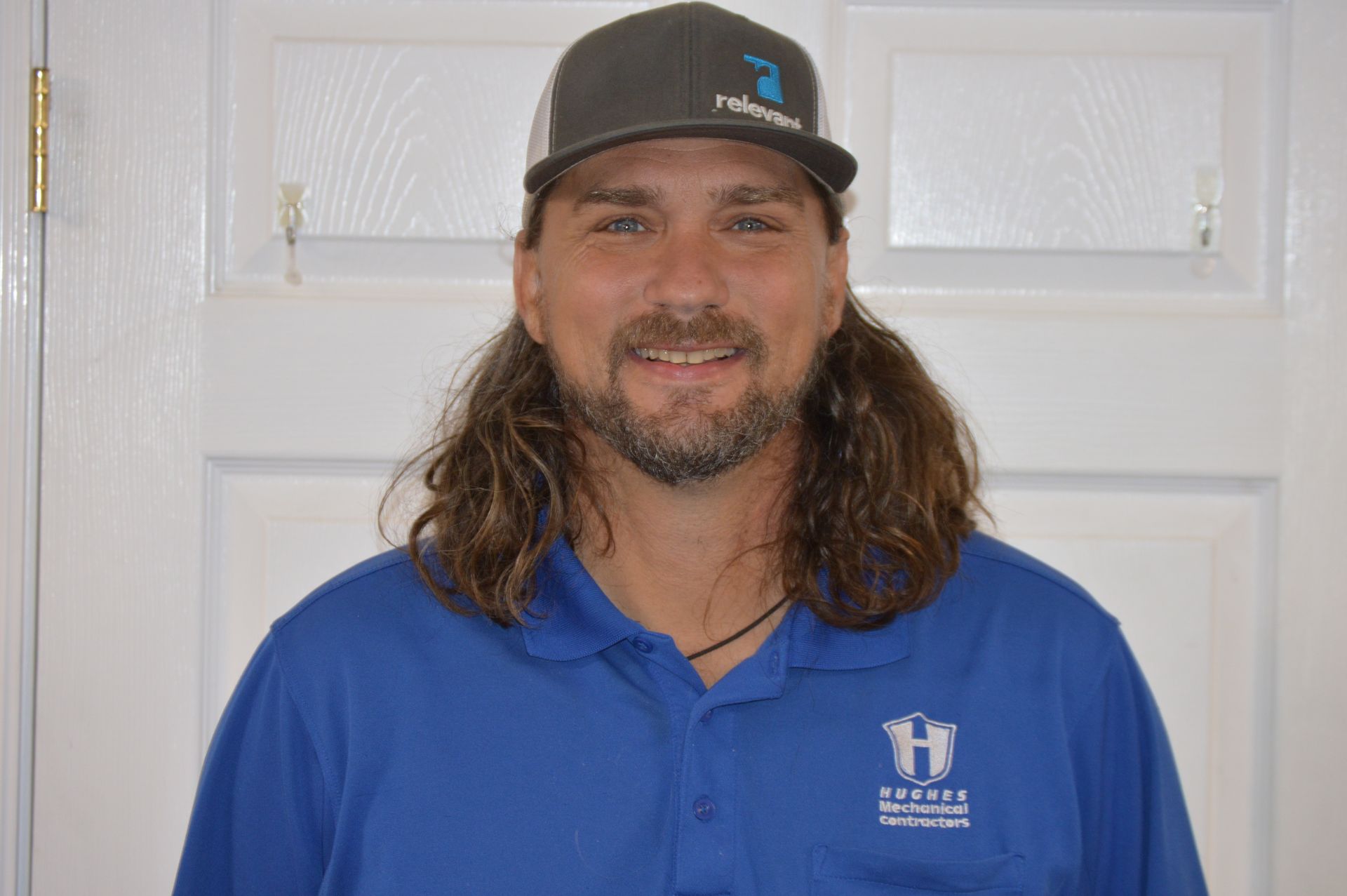 Man in blue polo and cap smiles in front of a white door.