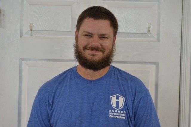 Man with beard wearing a blue shirt smiles in front of a white door.