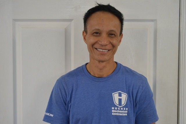 Man in blue t-shirt smiles in front of a white door. The shirt has a logo.