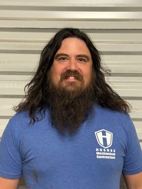 Man with long brown hair and beard wearing a blue shirt with a company logo, smiling.