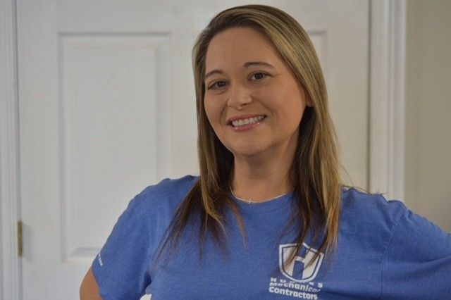 Woman in blue shirt smiles indoors near a white door.