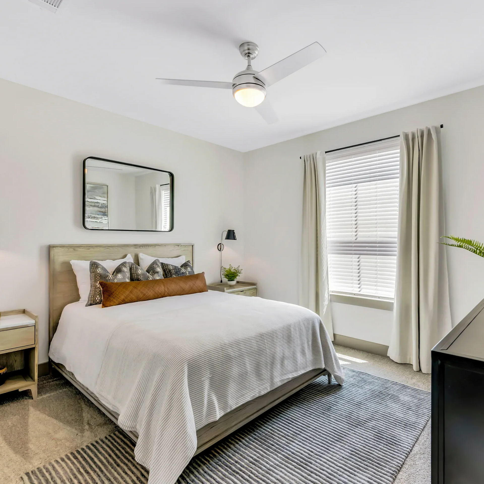 Bedroom with bed, mirror, window, and ceiling fan. Gray and white color scheme.