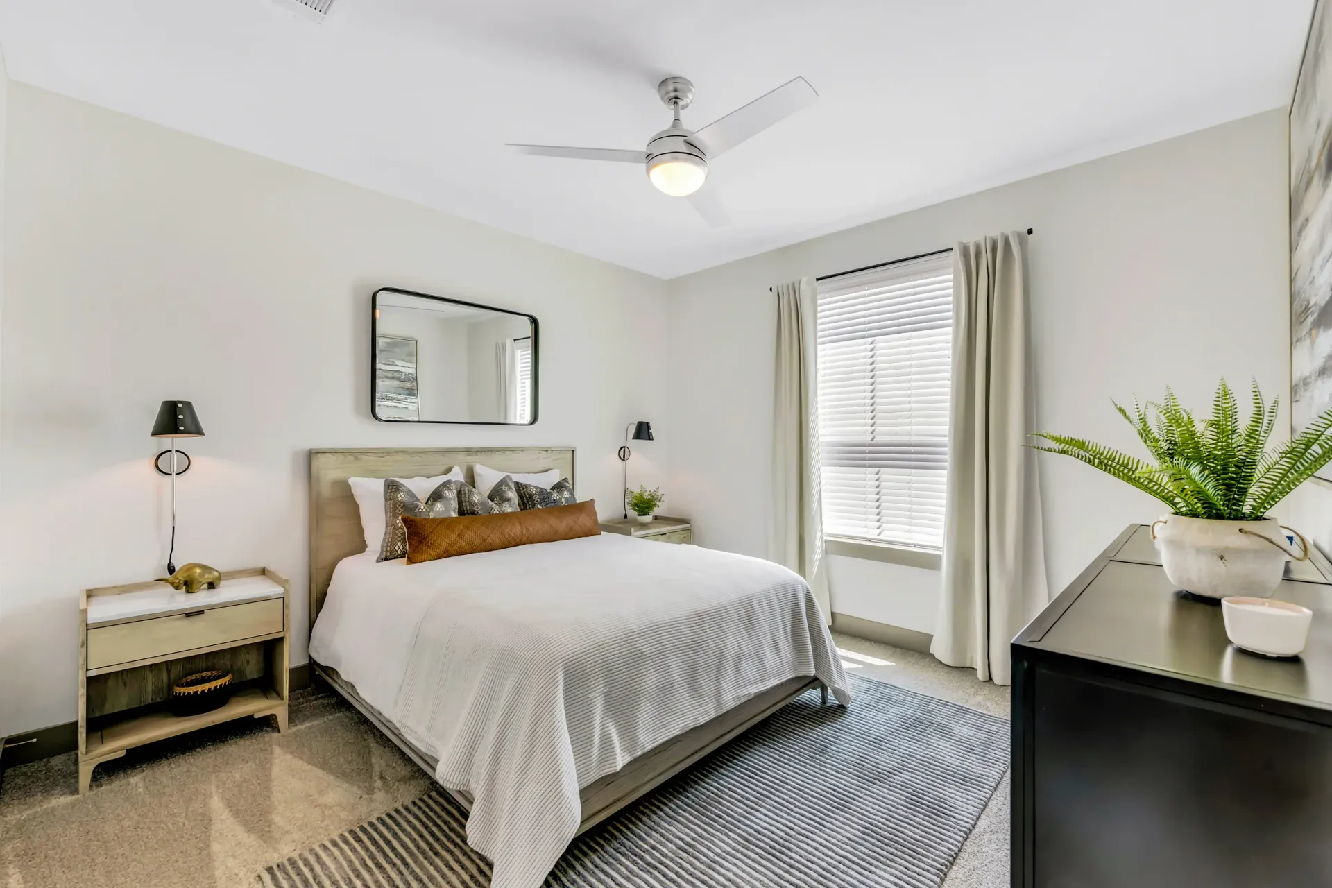 A bedroom with a large bed , a ceiling fan , a mirror and a sliding glass door at Atlas Bluewood in Celina, TX.
